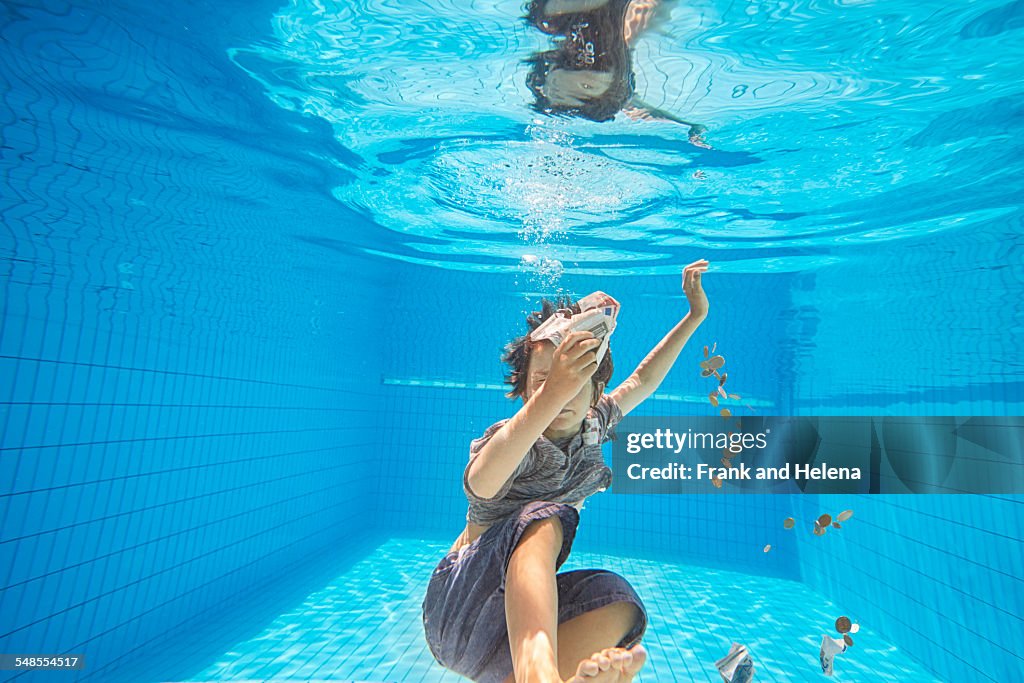 Underwater view of boy in swimming pool grabbing euro notes and coins