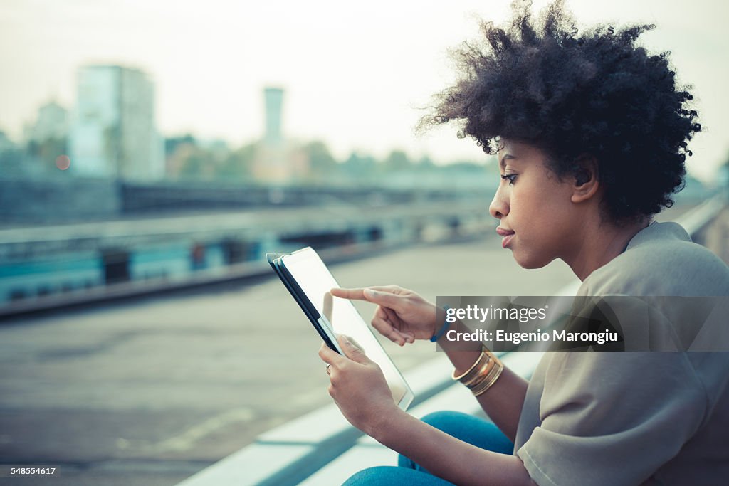 Young woman using touchscreen on digital tablet on city rooftop