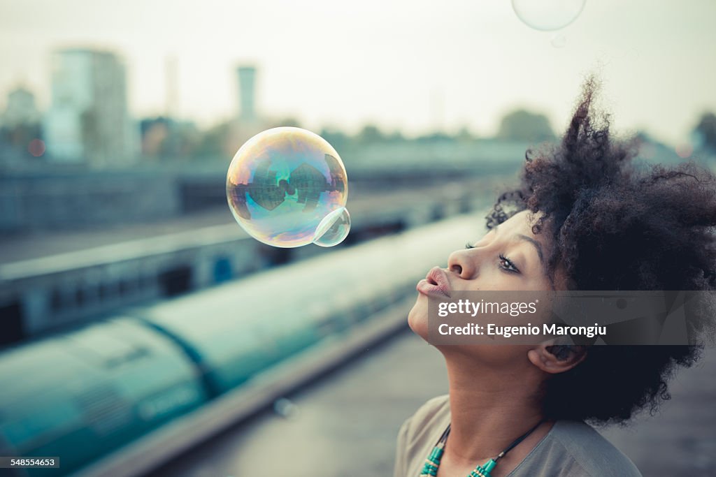 Young woman blowing bubbles in city industrial area