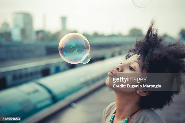 young woman blowing bubbles in city industrial area - bubble wand ストックフォトと画像