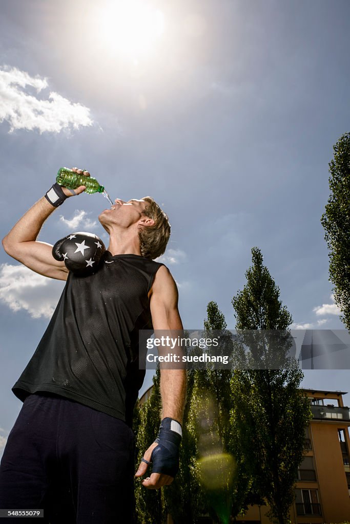 Mid adult male boxer drinking bottled water in park