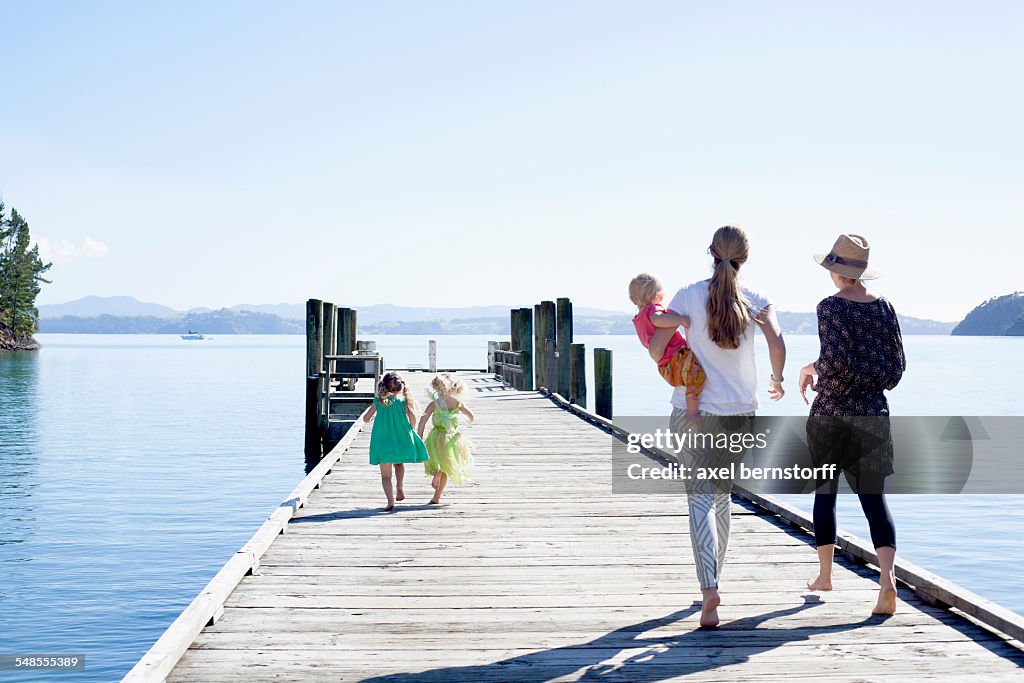 Two mid adult women and daughters strolling on pier, New Zealand