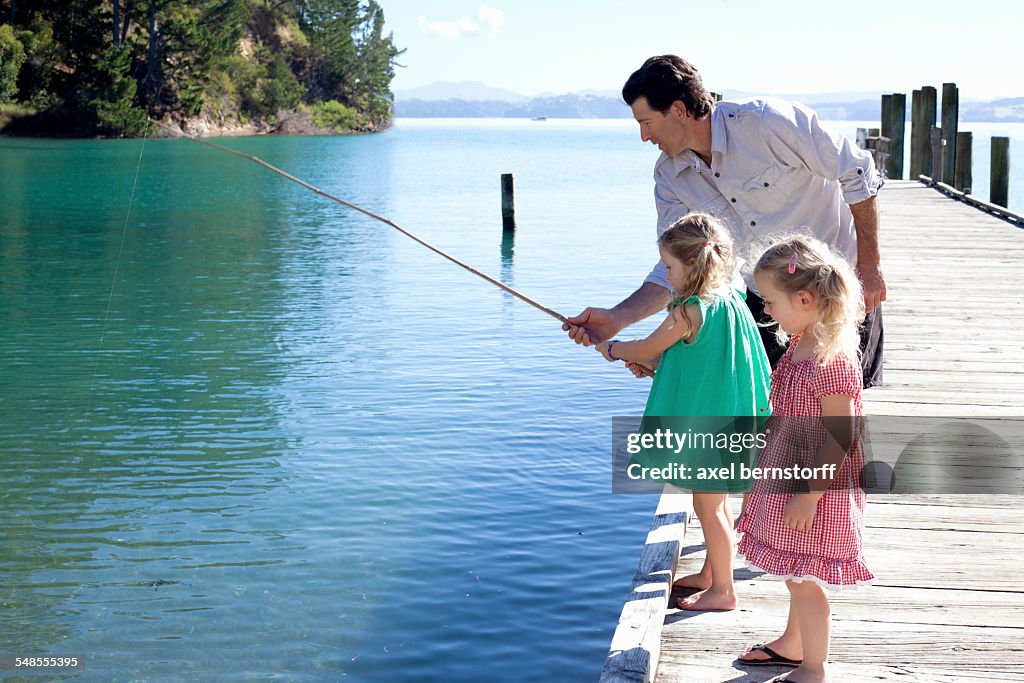 Mature man and two young girls fishing from pier, New Zealand