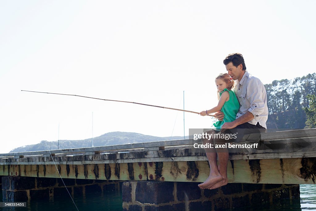 Mature man and daughter fishing on sea pier, New Zealand