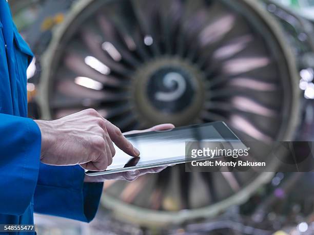 engineer using digital tablet in front of jet engine in aircraft maintenance factory - vehículo aéreo fotografías e imágenes de stock
