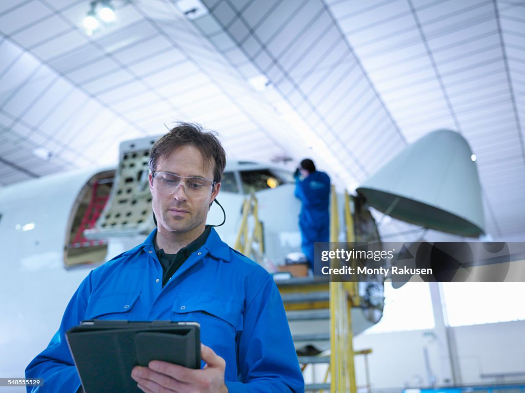 Engineer using digital tablet in aircraft maintenance factory
