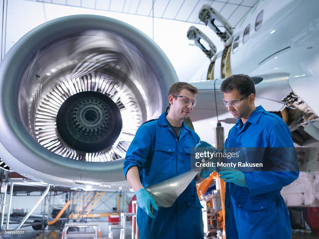 Engineers inspecting jet engine turbine blade in aircraft maintenance factory