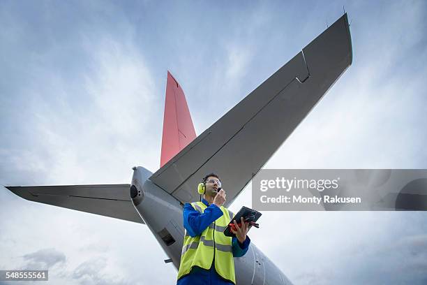 airside engineer talking on radio near aircraft on runway, low angle view - aviation hat stock-fotos und bilder