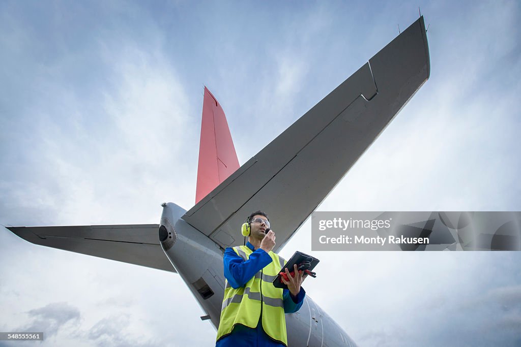Airside engineer talking on radio near aircraft on runway, low angle view