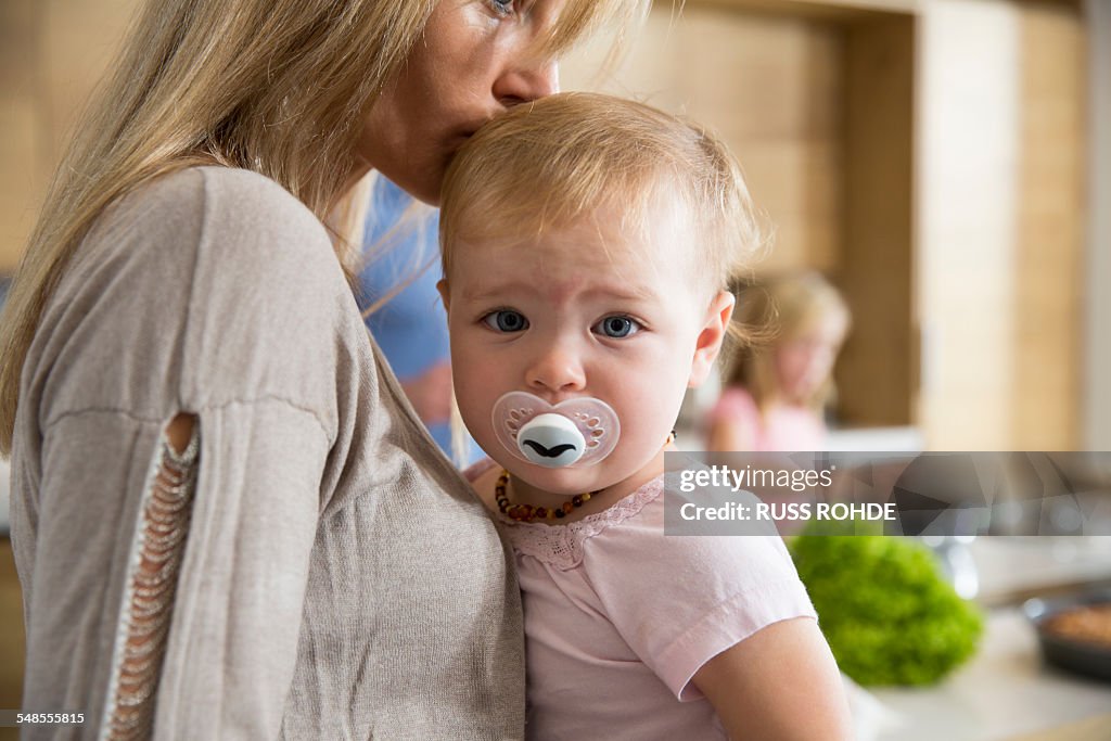 Portrait of female toddler in mothers arms in kitchen