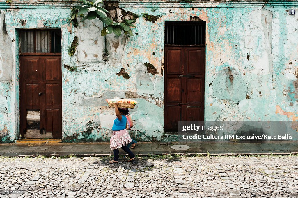 Woman carrying tray on head walking by house, Antigua, Guatemala