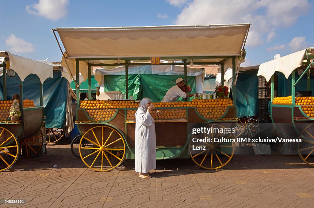 Moroccan woman drinking fresh orange juice from vendor, Djemaa el Fna Square, Marrakech, Morocco