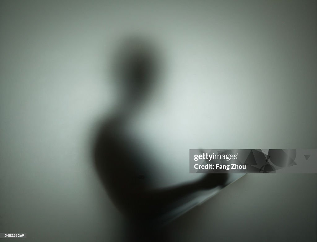 Silhouette of person using pen and clipboard, behind glass