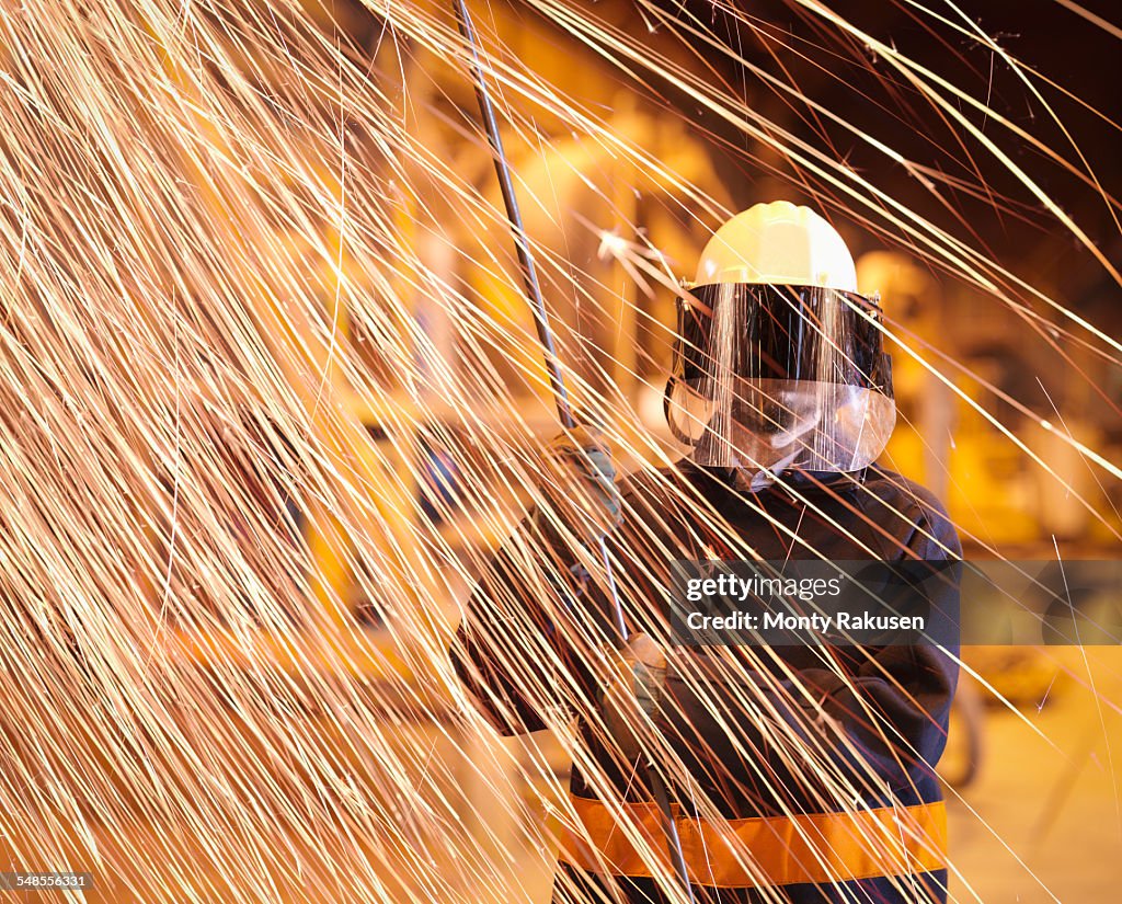 Steelworker holding sample lance behind sparks in steelworks