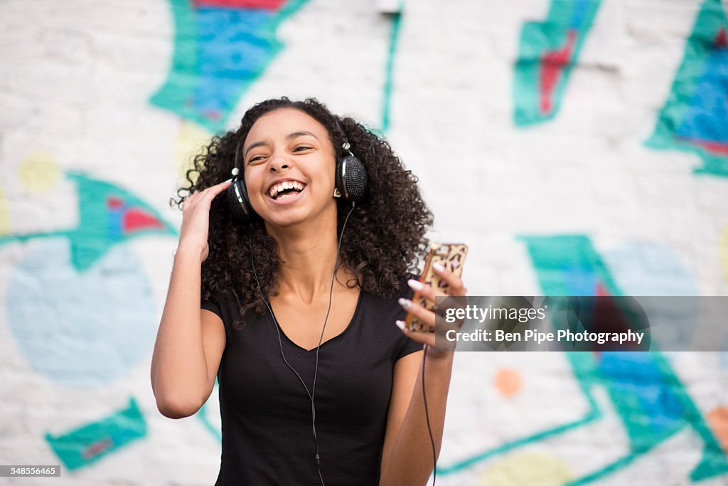 Teenager listening to mp3 player against wall with graffiti