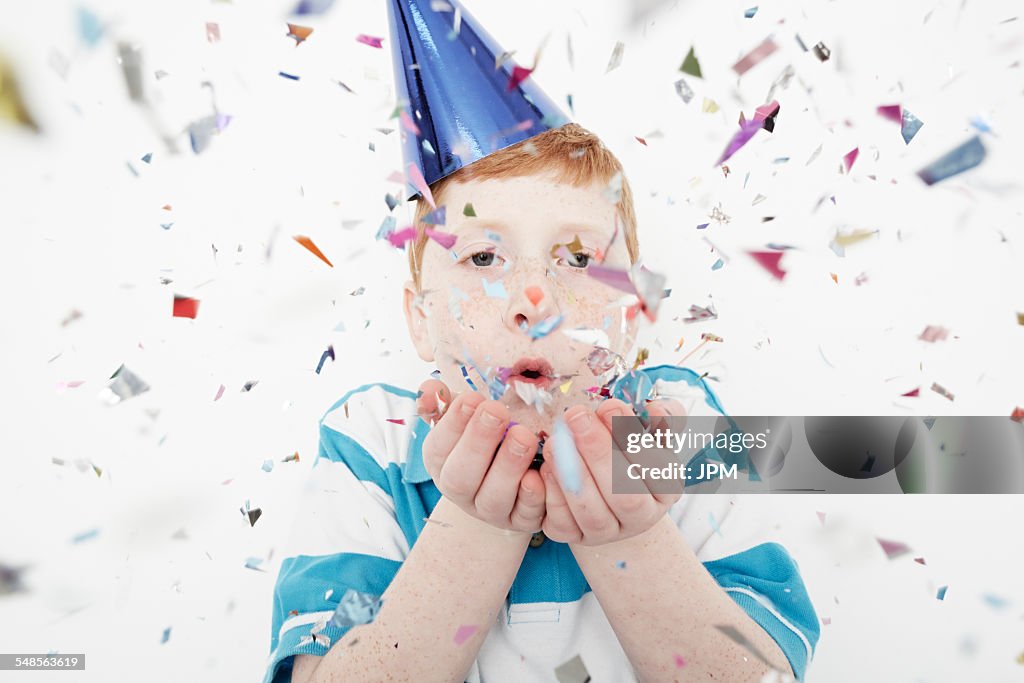 Boy wearing cone party hat blowing confetti