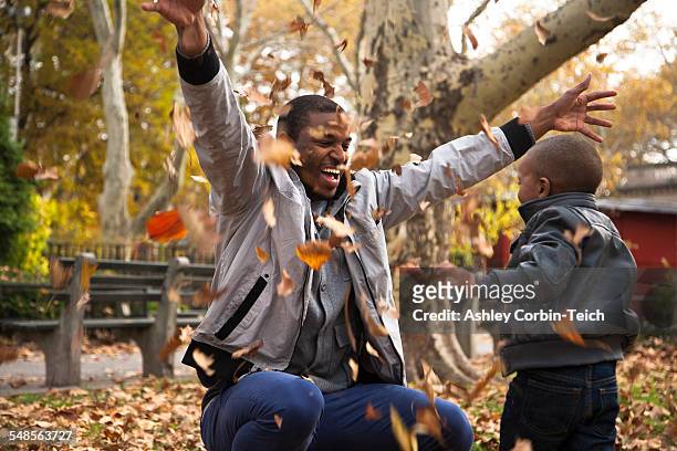 young man and toddler son throwing autumn leaves in park - autumn in new york foto e immagini stock
