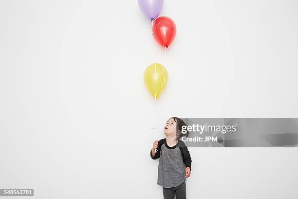 portrait of cute male toddler holding and gazing up at three helium balloons - child balloon studio photos et images de collection