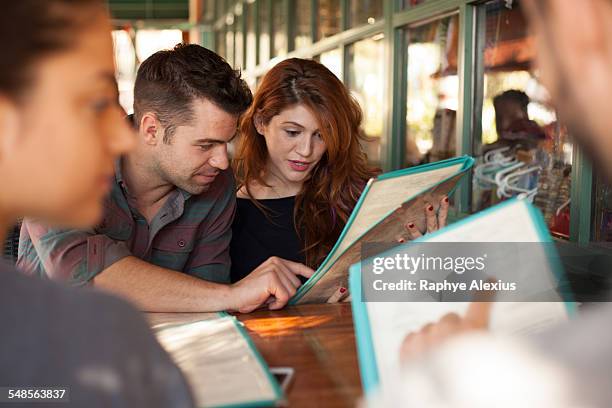 four friends looking at menus in vegetarian restaurant - speisekarte stock-fotos und bilder