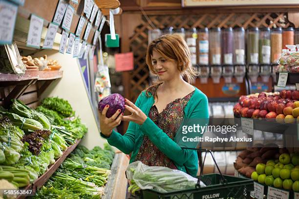 mid adult woman selecting red cabbage in health food store - produce aisle photos et images de collection