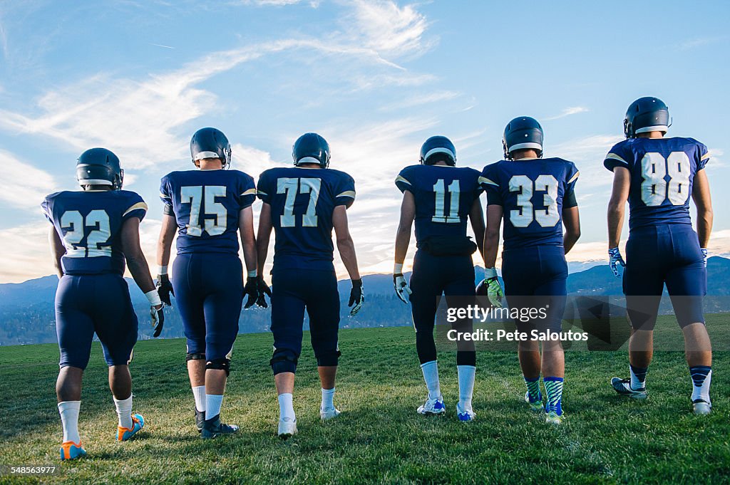 Rear view of teenage and young adult american football team in a row