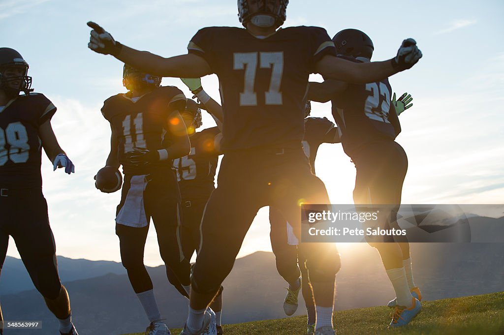 Silhouetted teenage and young male american football team celebrating at sunset