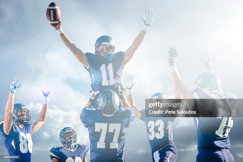 Teenage and young male American football team celebrating on pitch