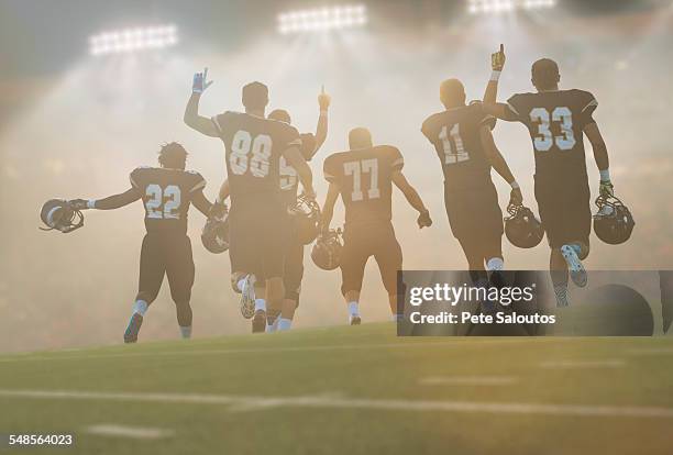 rear view of teenage and young male american football team celebrating in stadium - blue shirt back stock pictures, royalty-free photos & images