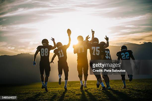 rear view of teenage and young male american football team celebrating at sunset - american football sport stock-fotos und bilder