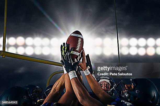 victorious teenage and young male american football team holding up ball at night - american football ストックフォトと画像