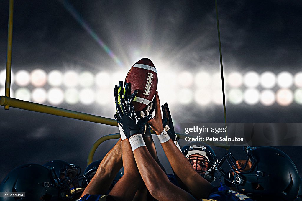 Victorious teenage and young male american football team holding up ball at night