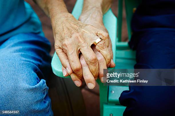 cropped close up of senior couple hands holding on park bench - old couple love stock-fotos und bilder