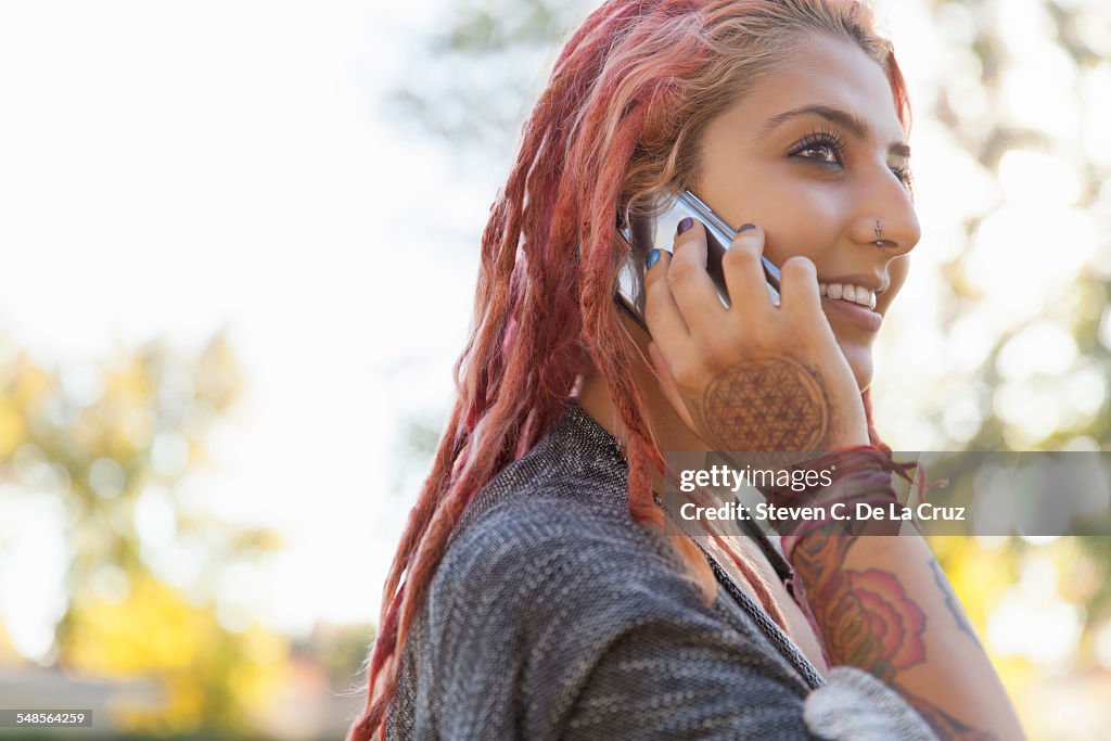 Young woman with pink dreadlocks chatting on smartphone in park