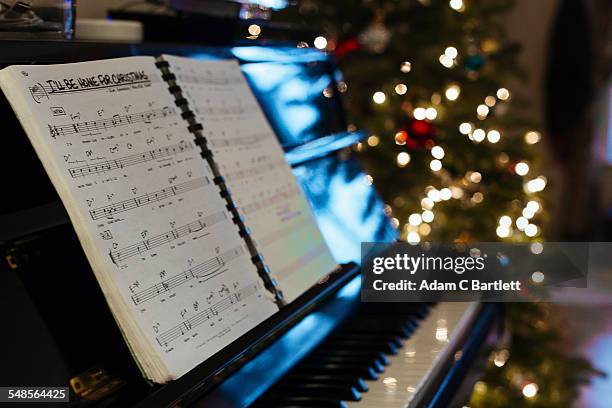 sheet music on piano, christmas tree in background - christmas music stock pictures, royalty-free photos & images