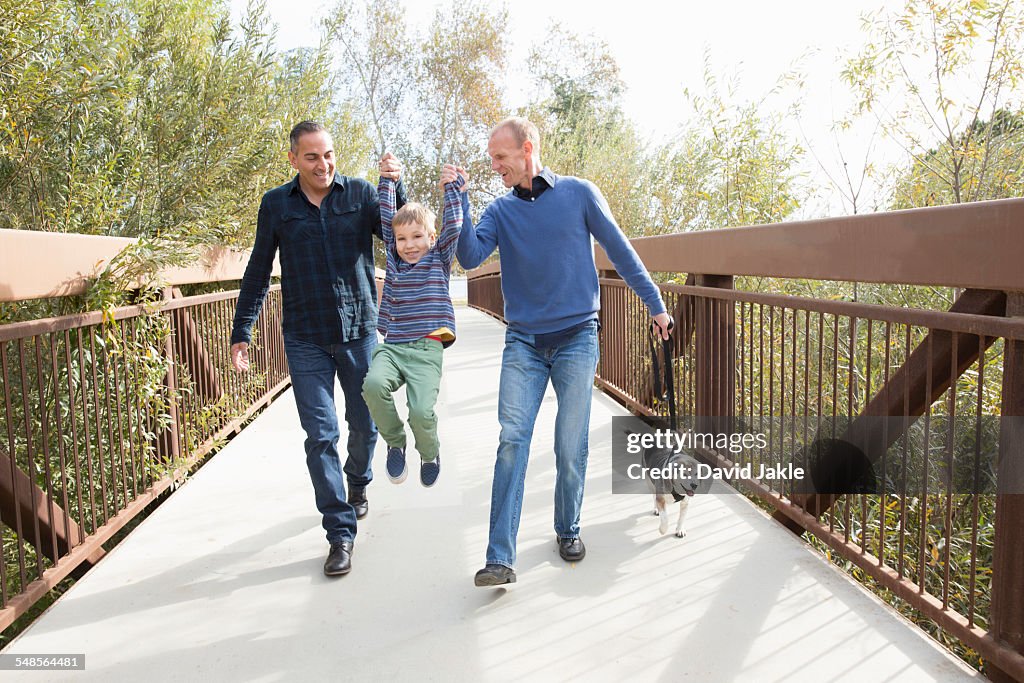 Male couple lifting up son and walking dog in park