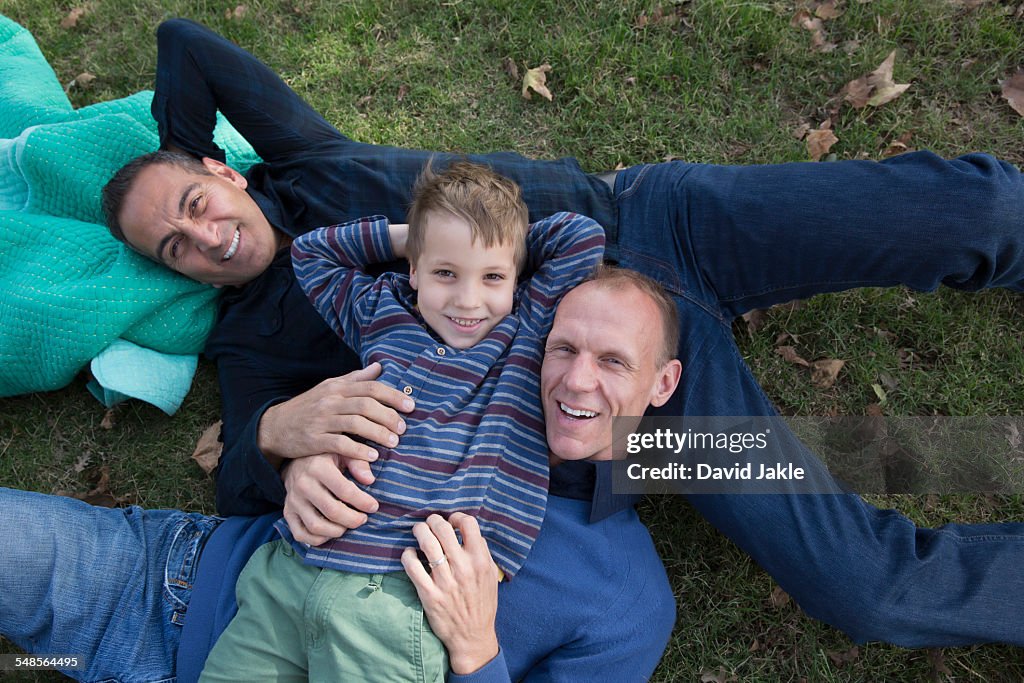 Portrait of male couple and son lying on backs in park