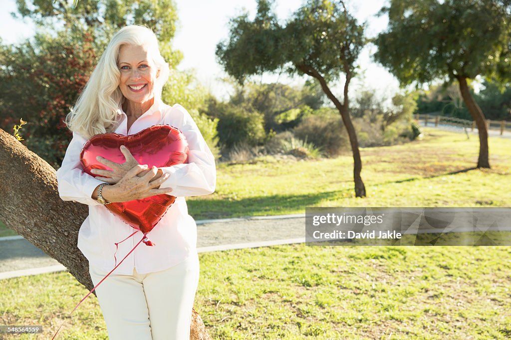 Senior woman hugging red heart-shaped balloon, Hahn Park, Los Angeles, California, USA