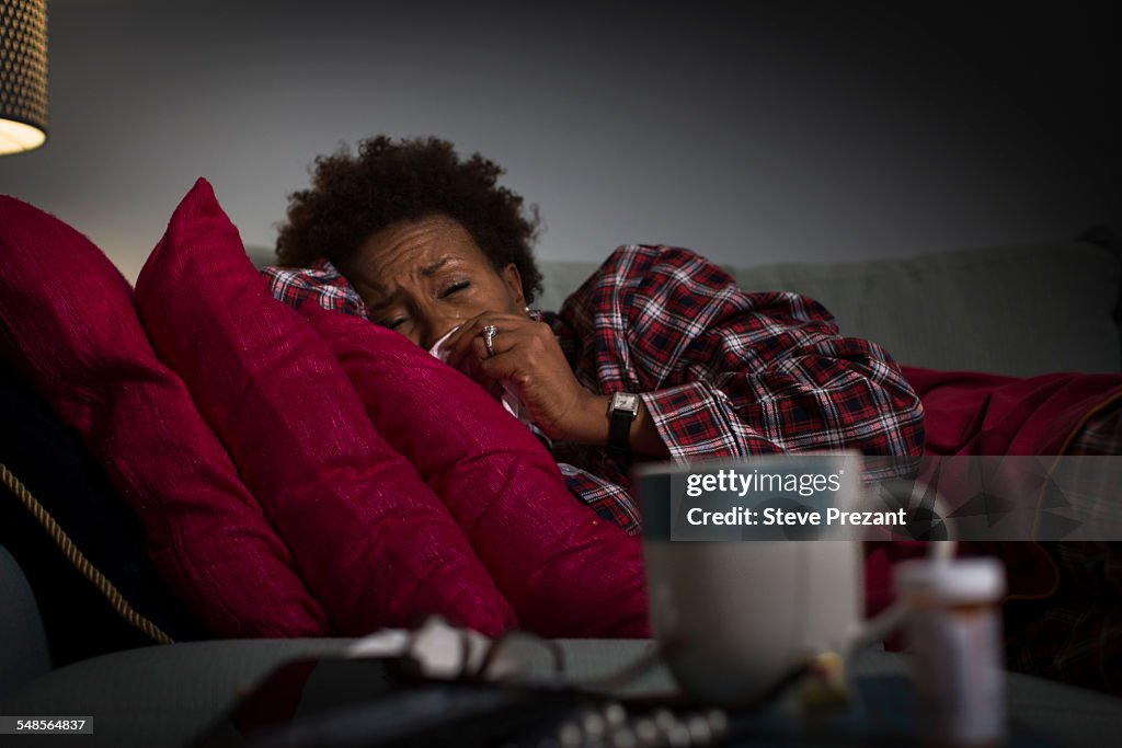 Mature woman with cold lying on couch