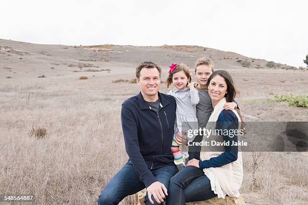 portrait of parents and two children sitting on rock - front view portrait of four children sitting on rock stock-fotos und bilder