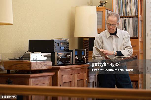 senior man reading vinyl record cover in living room - album covers fotografías e imágenes de stock