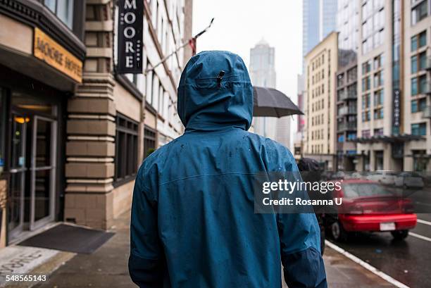 rear view of young man strolling on rainy street, seattle, washington state, usa - gabardina ropa impermeable fotografías e imágenes de stock