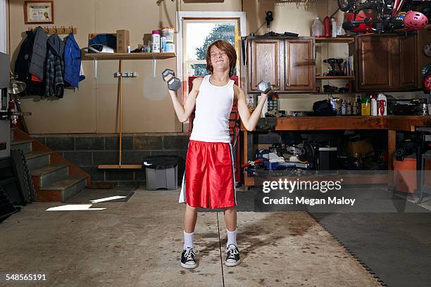 slim boy struggling to lift hand weights in garage - skinny stock-fotos und bilder