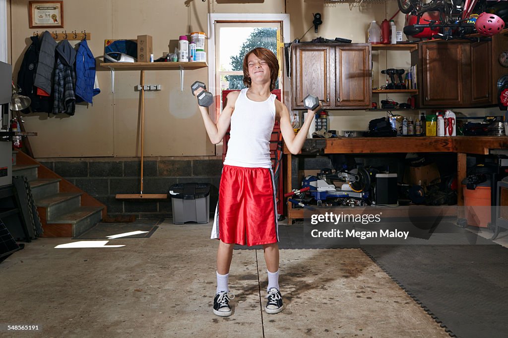 Slim boy struggling to lift hand weights in garage