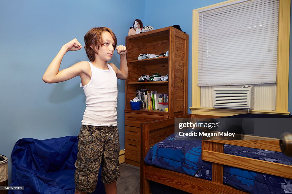 Slim boy flexing arm muscles in bedroom