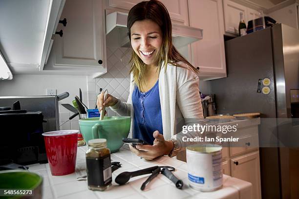 woman preparing food in kitchen whilst reading recipe from smartphone - woman cooking phone stock-fotos und bilder