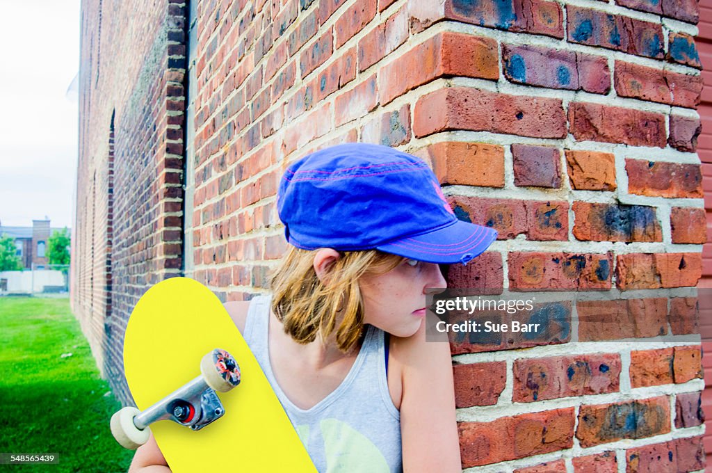 Tomboy skateboarder girl peeking around brick wall corner