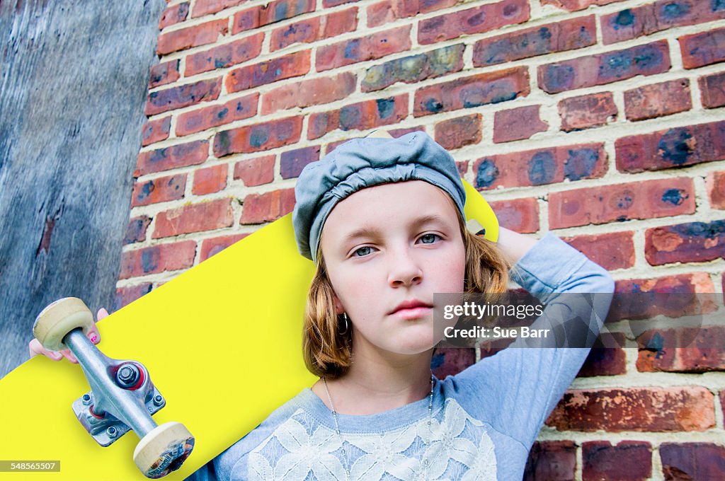 Portrait of sullen tomboy skateboarder girl leaning against brick wall