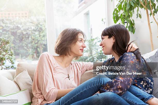 lesbian couple cuddled up, sitting on sofa. - leaninlgbt stock pictures, royalty-free photos & images