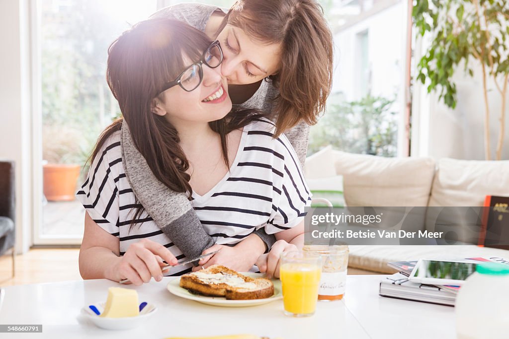 Woman kisses girlfriend eating breakfast.