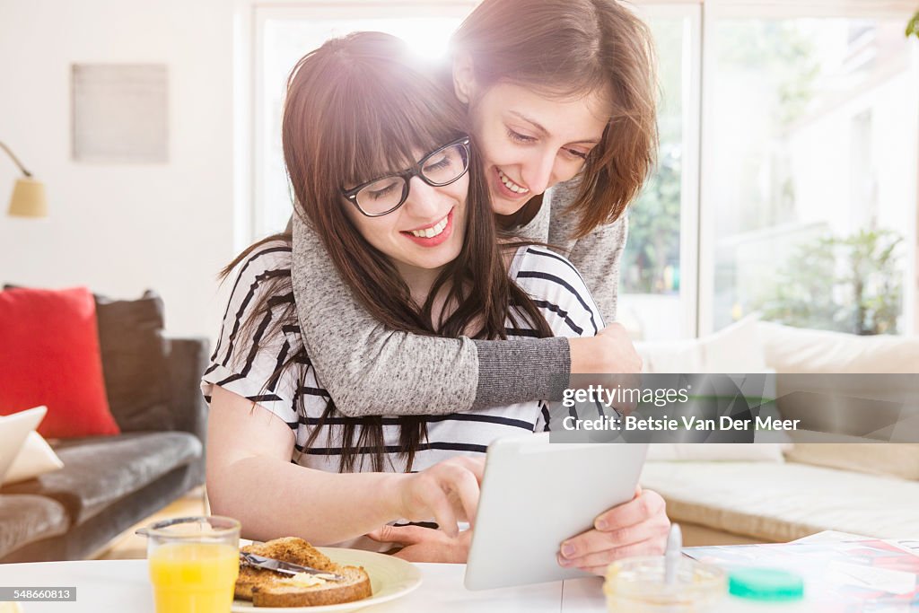 Woman embraces girlfriend looking a digital tablet